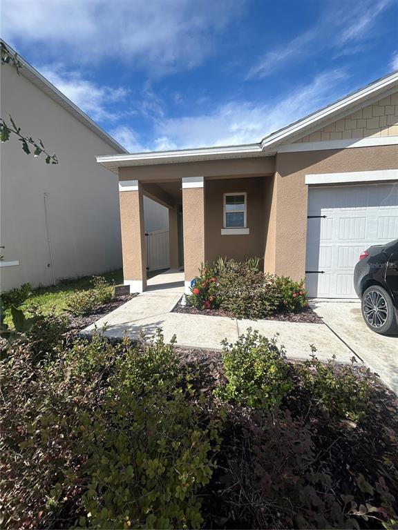 A tan house exterior features a covered entryway, a garage, and a small front garden — 1396 BERRY LANE, DAVENPORT, FL