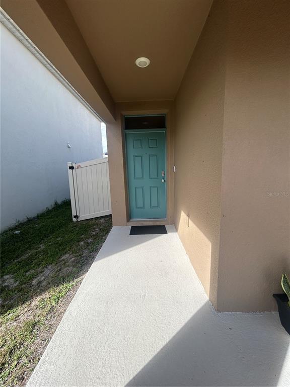 A teal front door is set within a covered concrete porch next to a fence — 1396 BERRY LANE, DAVENPORT, FL