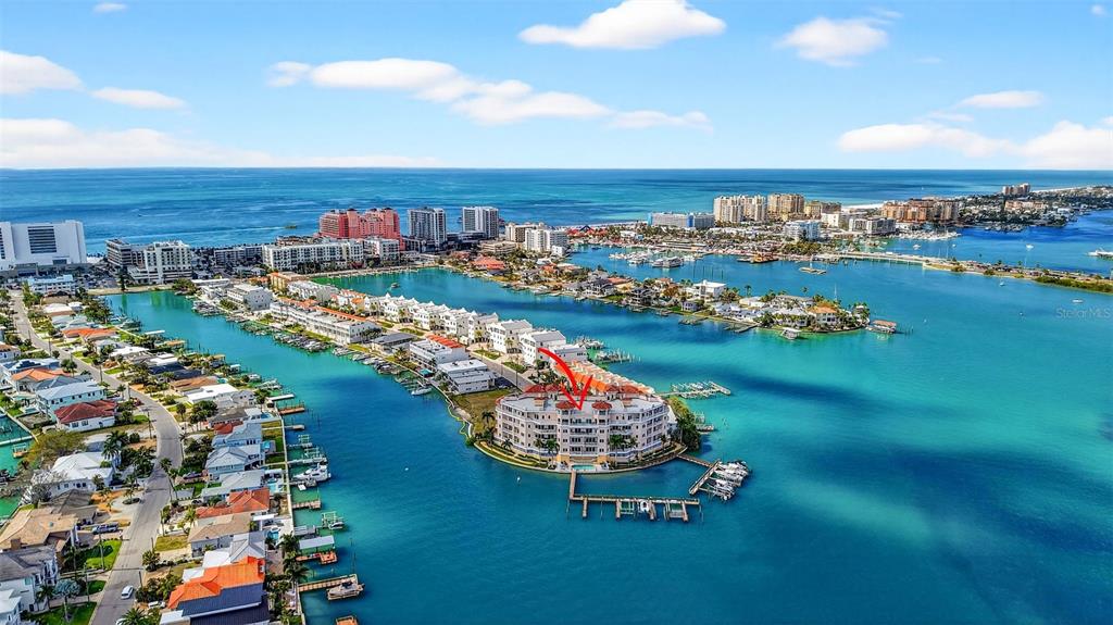 An aerial view shows a multi-story waterfront condominium building surrounded by a bay and residential homes — 205 BRIGHTWATER DRIVE UNIT 202, CLEARWATER BEACH, FL