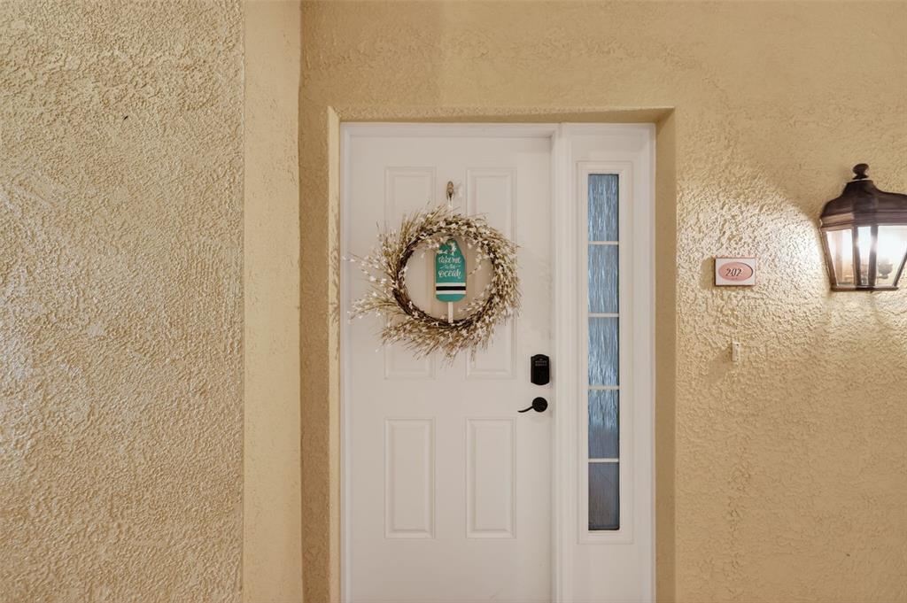 A white front door with a wreath and a side light on a stucco wall — 205 BRIGHTWATER DRIVE UNIT 202, CLEARWATER BEACH, FL