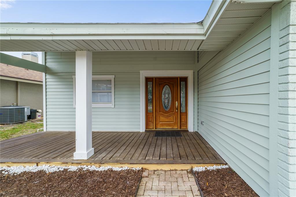 A wooden porch with a white pillar leads to a front door with glass inserts — 3149 N CANAL DRIVE, PALM HARBOR, FL