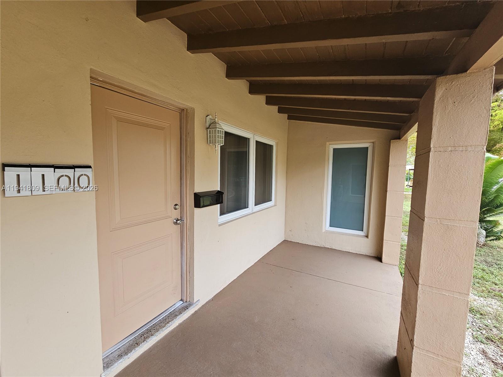 A covered porch features a beige door, a mailbox, and a concrete floor — 1100 NE 115 # 0, Biscayne Park FL 33161, BISCAYNE PARK, FL