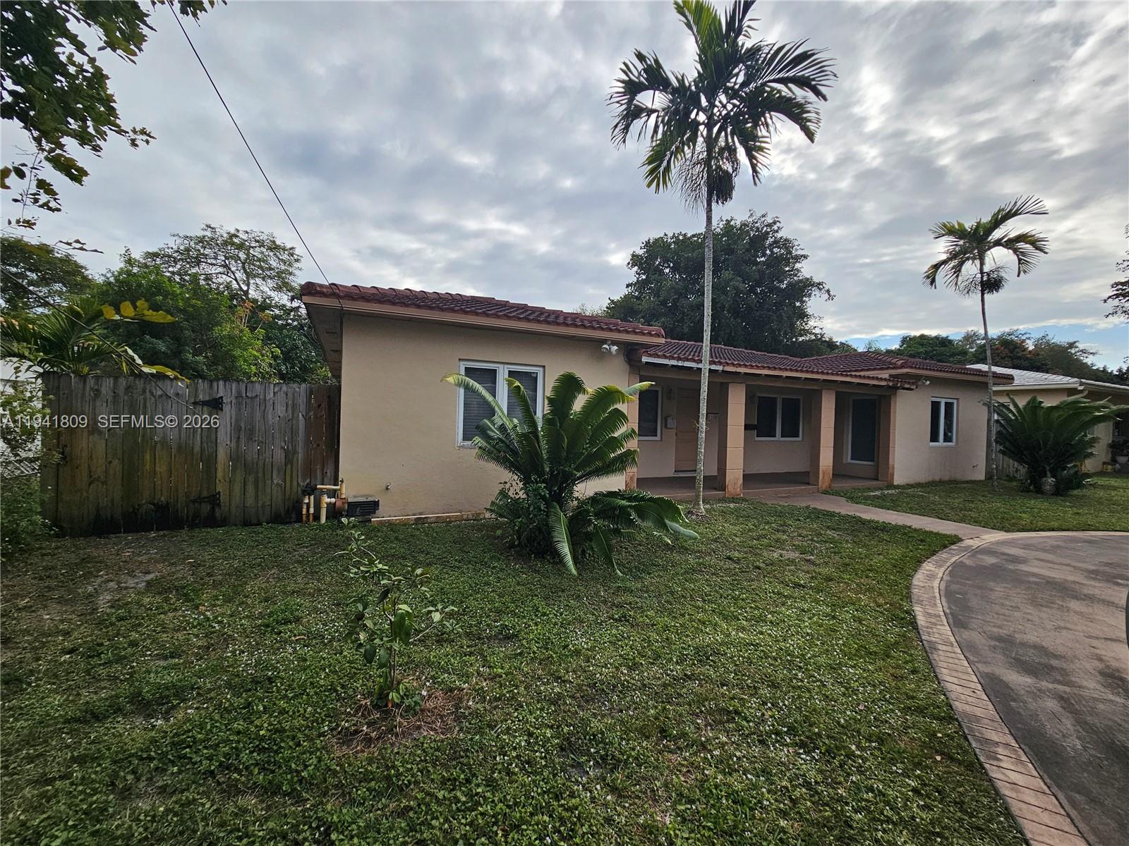 A single-story tan house with a tiled roof, palm trees, and a wooden fence — 1100 NE 115 # 0, Biscayne Park FL 33161, BISCAYNE PARK, FL