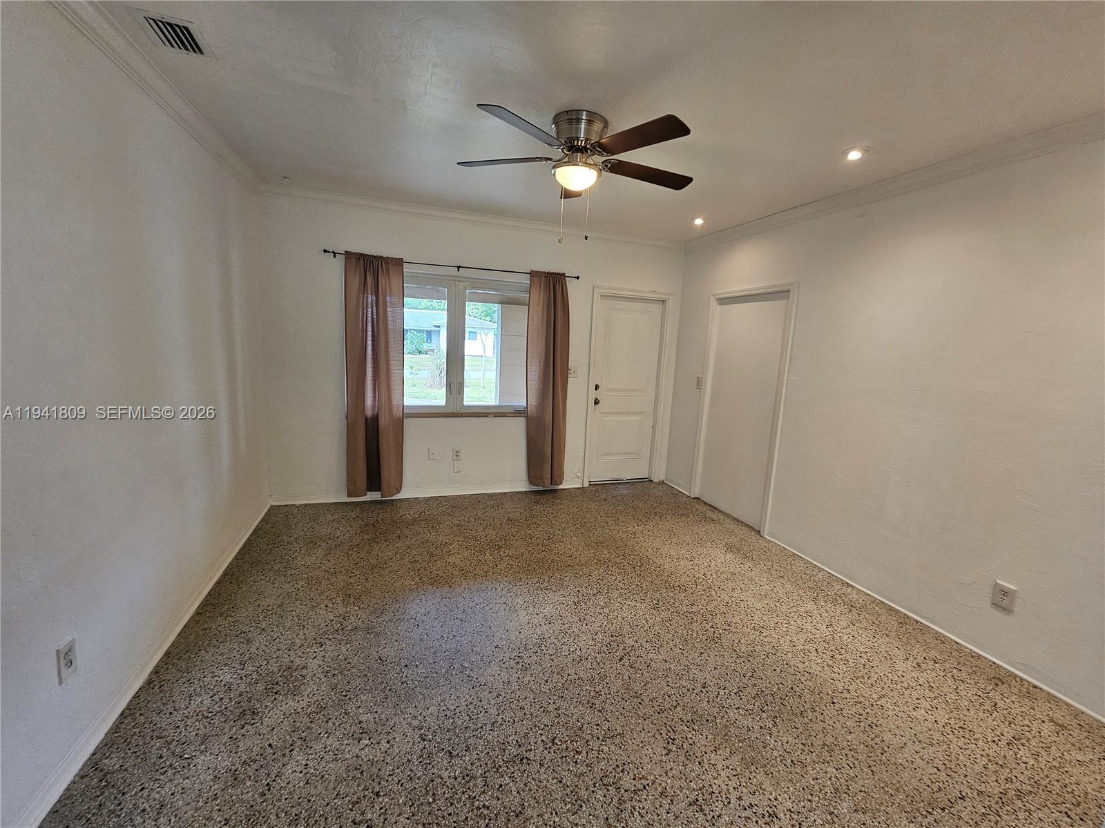 An empty room features white walls, a ceiling fan, and speckled wall-to-wall carpeting — 1100 NE 115 # 0, Biscayne Park FL 33161, BISCAYNE PARK, FL