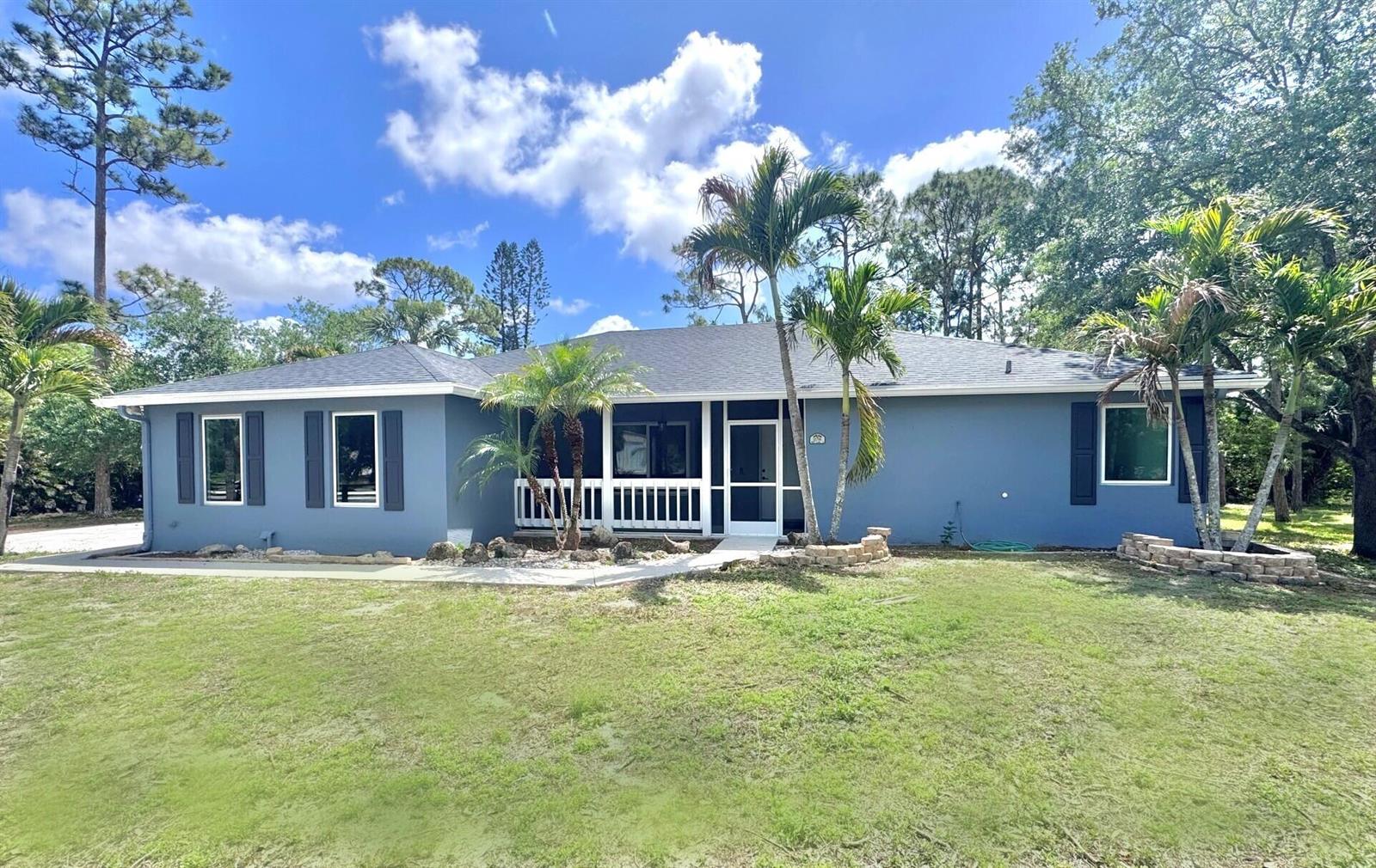 A single-story blue house with a screened front porch, dark shutters, and surrounding palm trees — 13706 N 41st Ln Lane N, FL 33411, FL