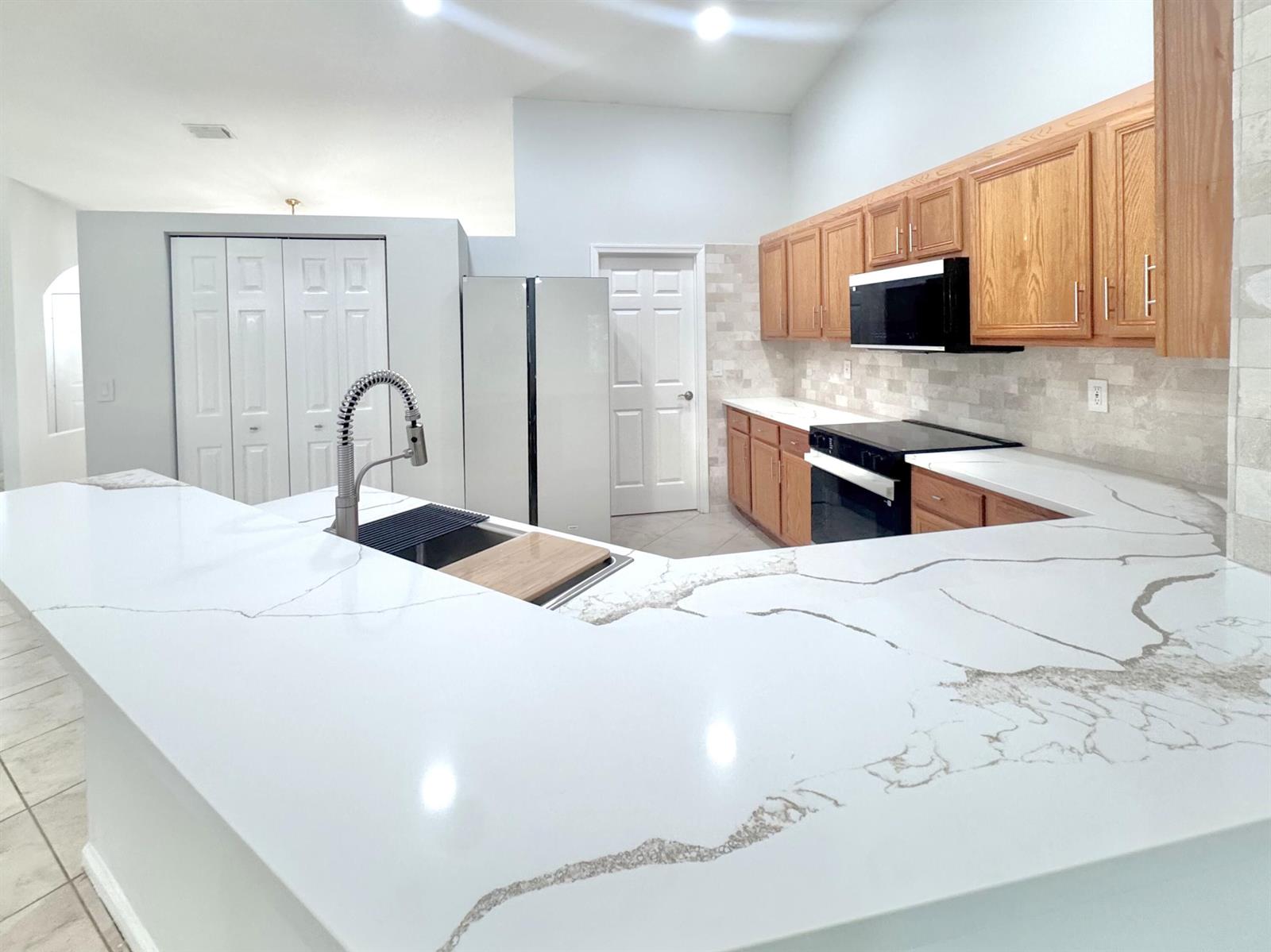 A kitchen features light wood cabinets, white marble-patterned countertops, and a large central island — 13706 N 41st Ln Lane N, FL 33411, FL