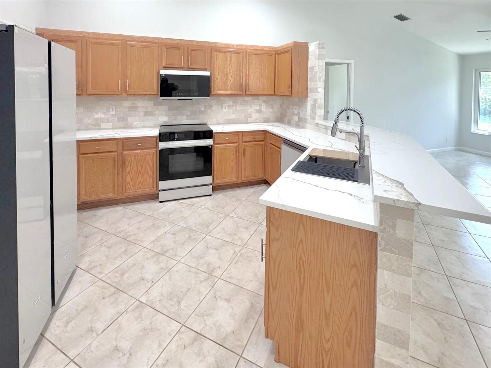 A kitchen features oak cabinets, white quartz countertops, a tile backsplash, and light floor tiles — 13706 N 41st Ln Lane N, FL 33411, FL