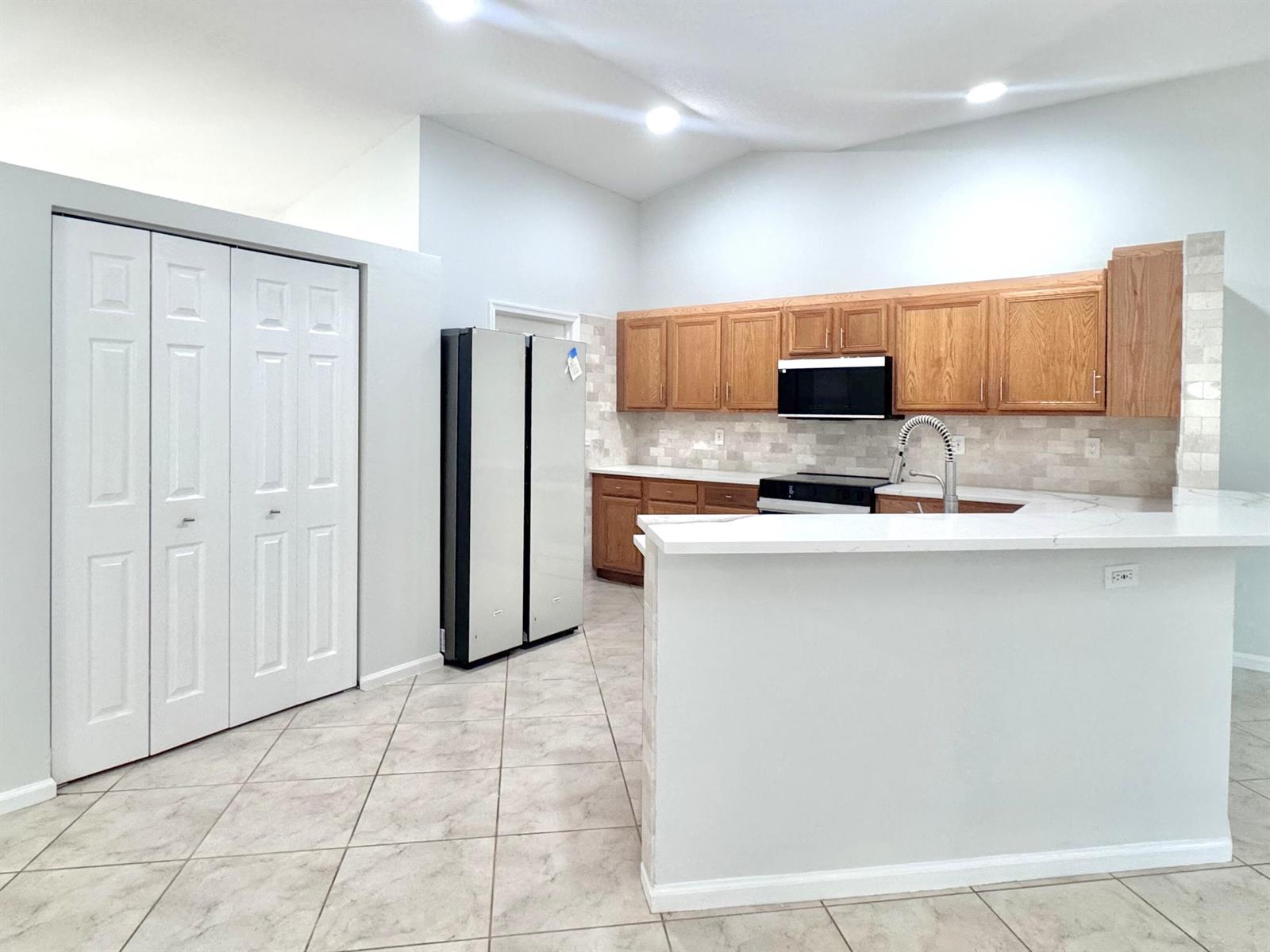 A kitchen features wood cabinets, white countertops, a tiled backsplash, and light-colored floor tiles — 13706 N 41st Ln Lane N, FL 33411, FL