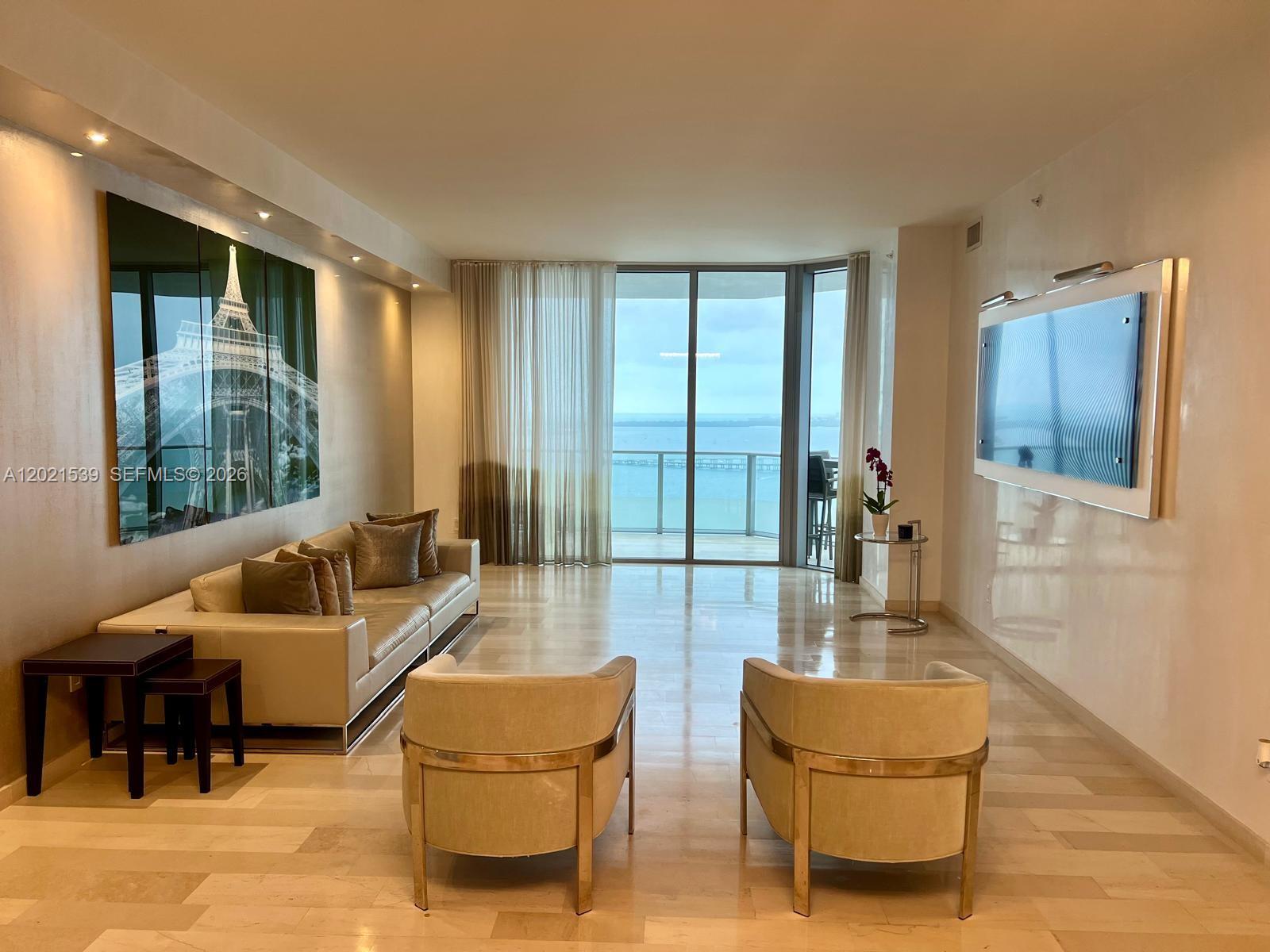 A living room features light wood floors, a large Eiffel Tower triptych, and floor-to-ceiling windows — 1300 E Brickell Bay Dr # 3701, Miami FL 33131, MIAMI, FL