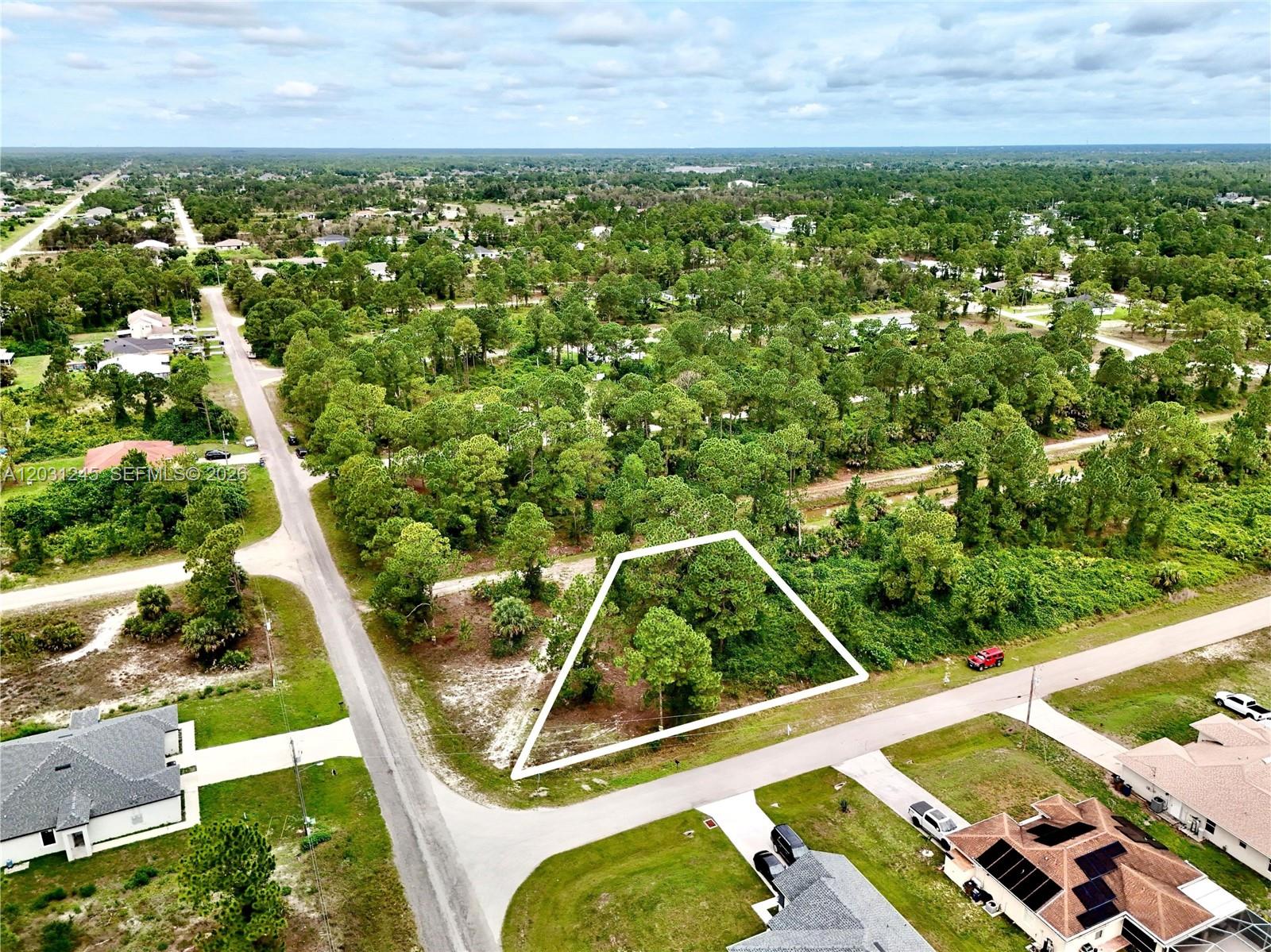 An aerial view shows a vacant, wooded lot outlined in white between two paved roads — 721 PINECASTLE DR, Lehigh Acres FL 33974, LEHIGH ACRES, FL