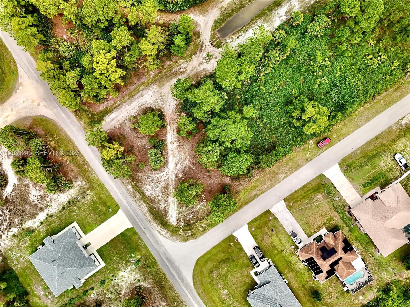 An aerial view shows a vacant corner lot surrounded by trees and residential houses — 721 PINECASTLE DR, Lehigh Acres FL 33974, LEHIGH ACRES, FL