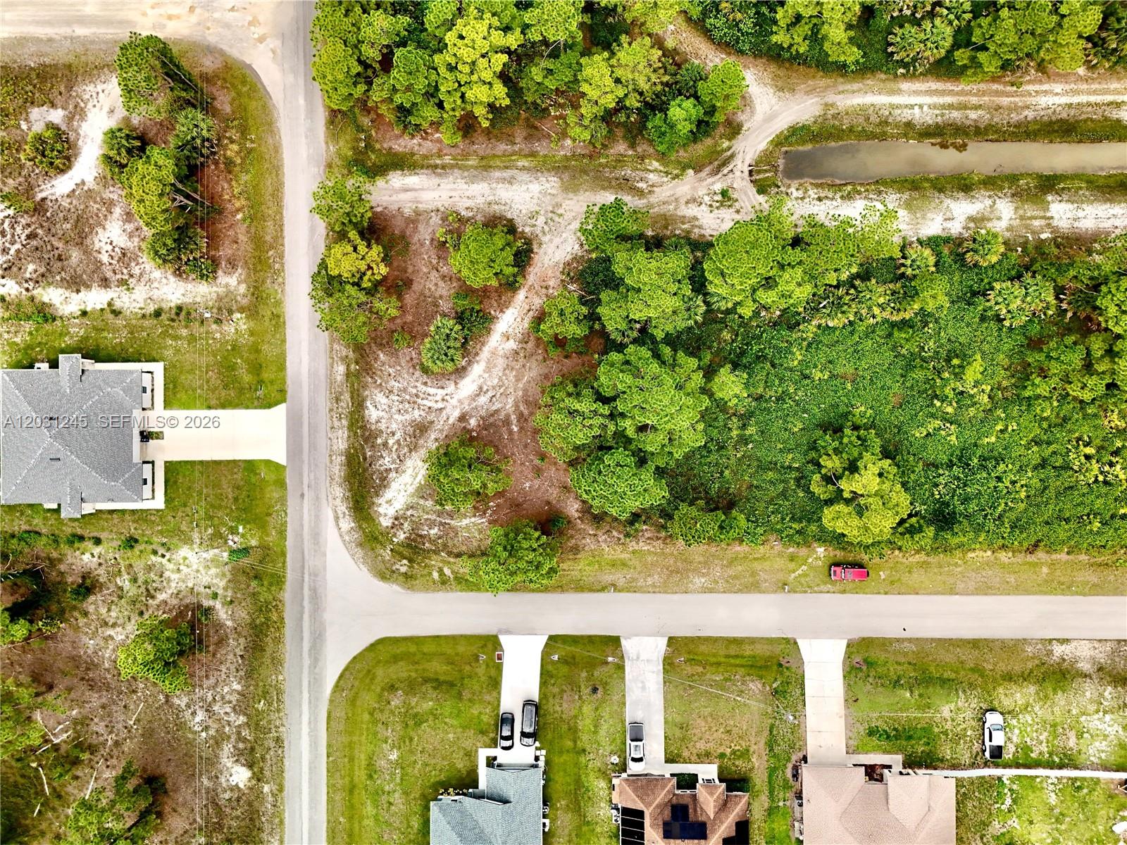 This aerial view shows a residential street with houses, vacant lots, and surrounding vegetation — 721 PINECASTLE DR, Lehigh Acres FL 33974, LEHIGH ACRES, FL