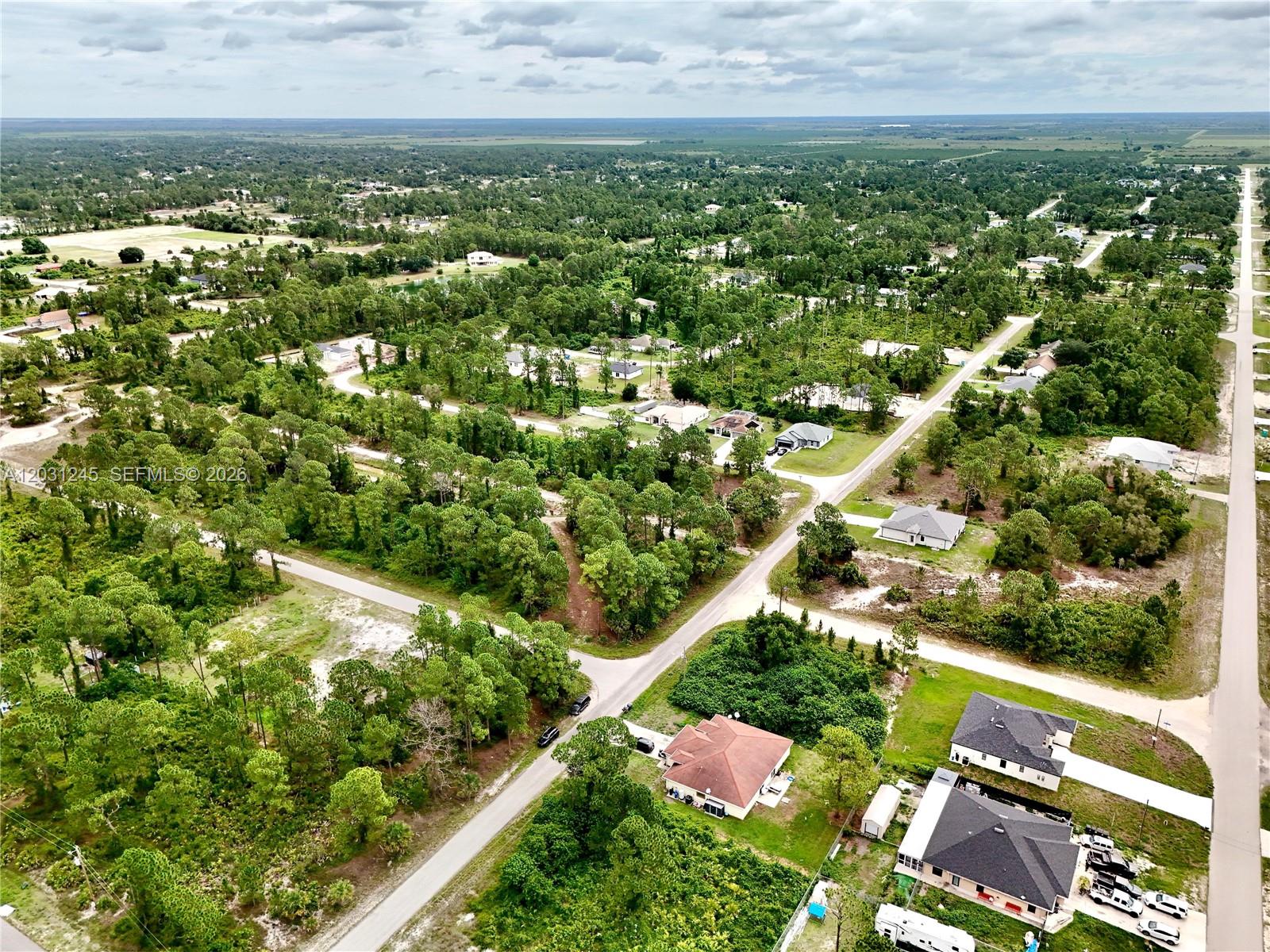 An aerial view shows houses scattered among dense trees and intersecting paved roads — 721 PINECASTLE DR, Lehigh Acres FL 33974, LEHIGH ACRES, FL