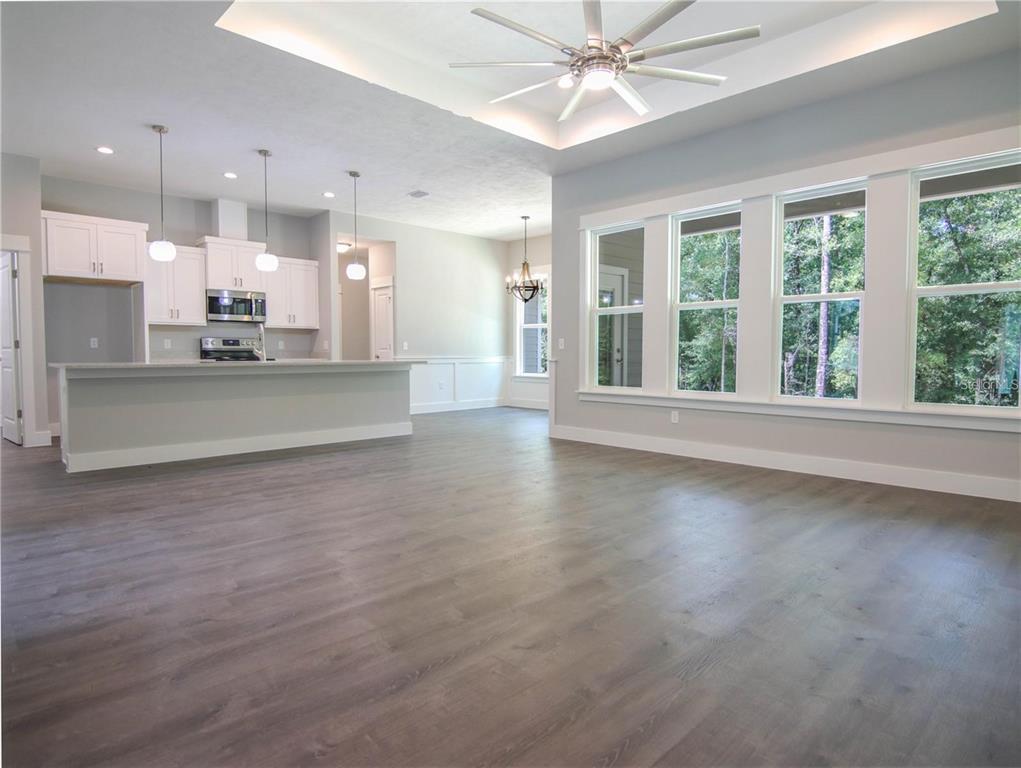 An open-concept kitchen and living area features gray wood-look flooring, white cabinetry, and large windows — 525 SW HEATHRIDGE DRIVE, LAKE CITY, FL