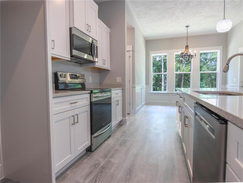 A modern kitchen features white cabinets, stainless steel appliances, and light wood-look flooring — 525 SW HEATHRIDGE DRIVE, LAKE CITY, FL