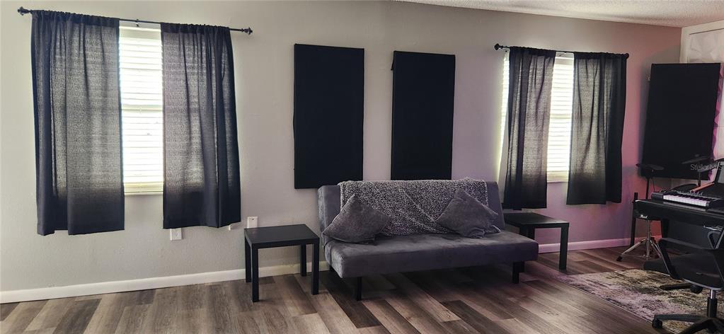 A room with wood-look flooring, a gray futon, black curtains, and wall-mounted acoustic panels — 6609 RIDGE ROAD UNIT 1, PORT RICHEY, FL