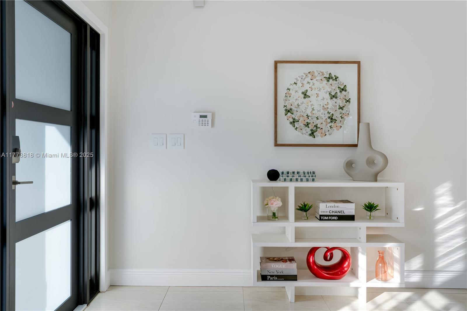A white entryway features a modern bookshelf, framed butterfly art, and a black-framed glass door — 14517 SW 98th Ter, Miami FL 33186, MIAMI, FL