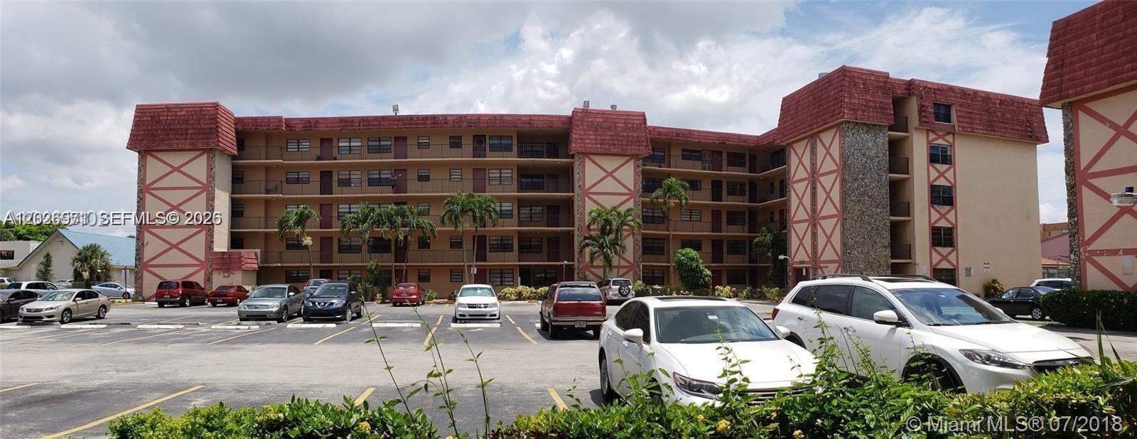 A multi-story apartment building with a red mansard roof sits behind a parking lot — 1325 W 68th St # 214, Hialeah FL 33014, HIALEAH, FL