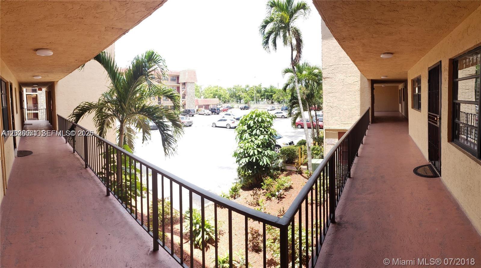 An outdoor apartment building walkway overlooks a parking lot with palm trees — 1325 W 68th St # 214, Hialeah FL 33014, HIALEAH, FL