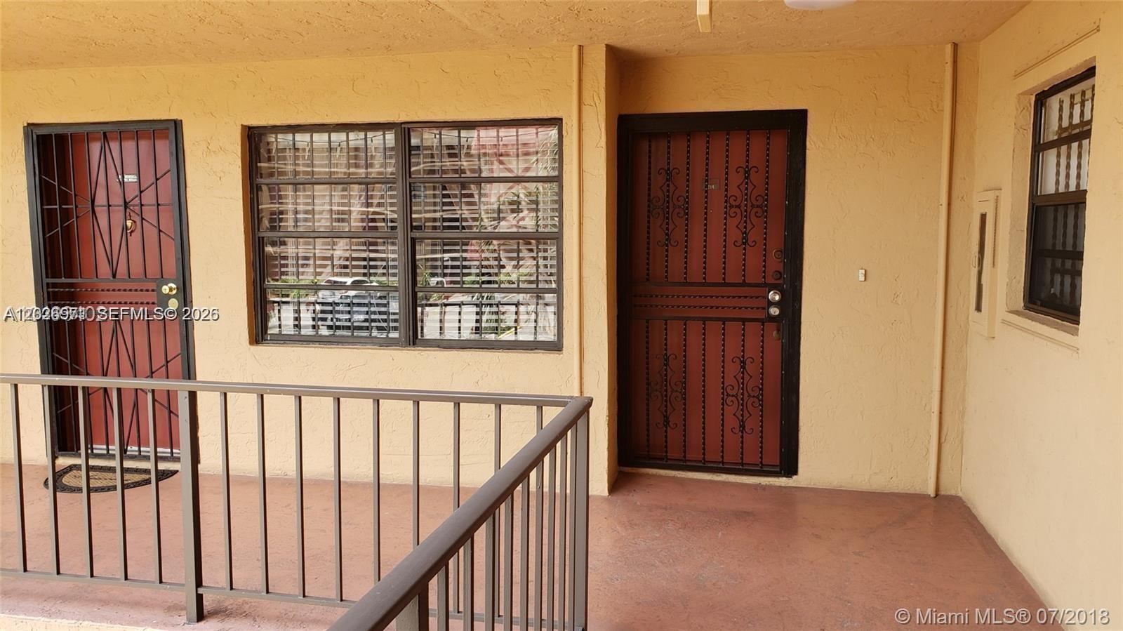 An exterior walkway features two doors with security grates and a large window — 1325 W 68th St # 214, Hialeah FL 33014, HIALEAH, FL