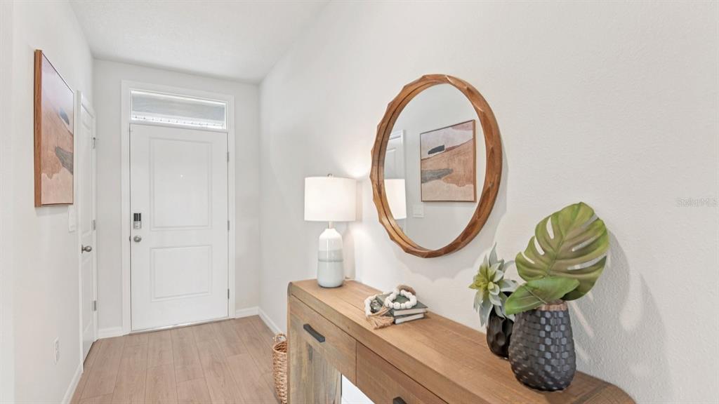 A bright entryway features a wooden console table, a round mirror, and a white door — 1209 12TH STREET SE, RUSKIN, FL