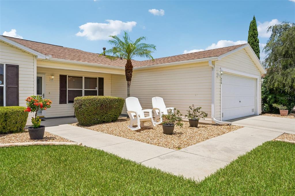 A single-story house with light siding, a garage, and two white chairs on gravel — 970 KENOVA AVENUE, THE VILLAGES, FL