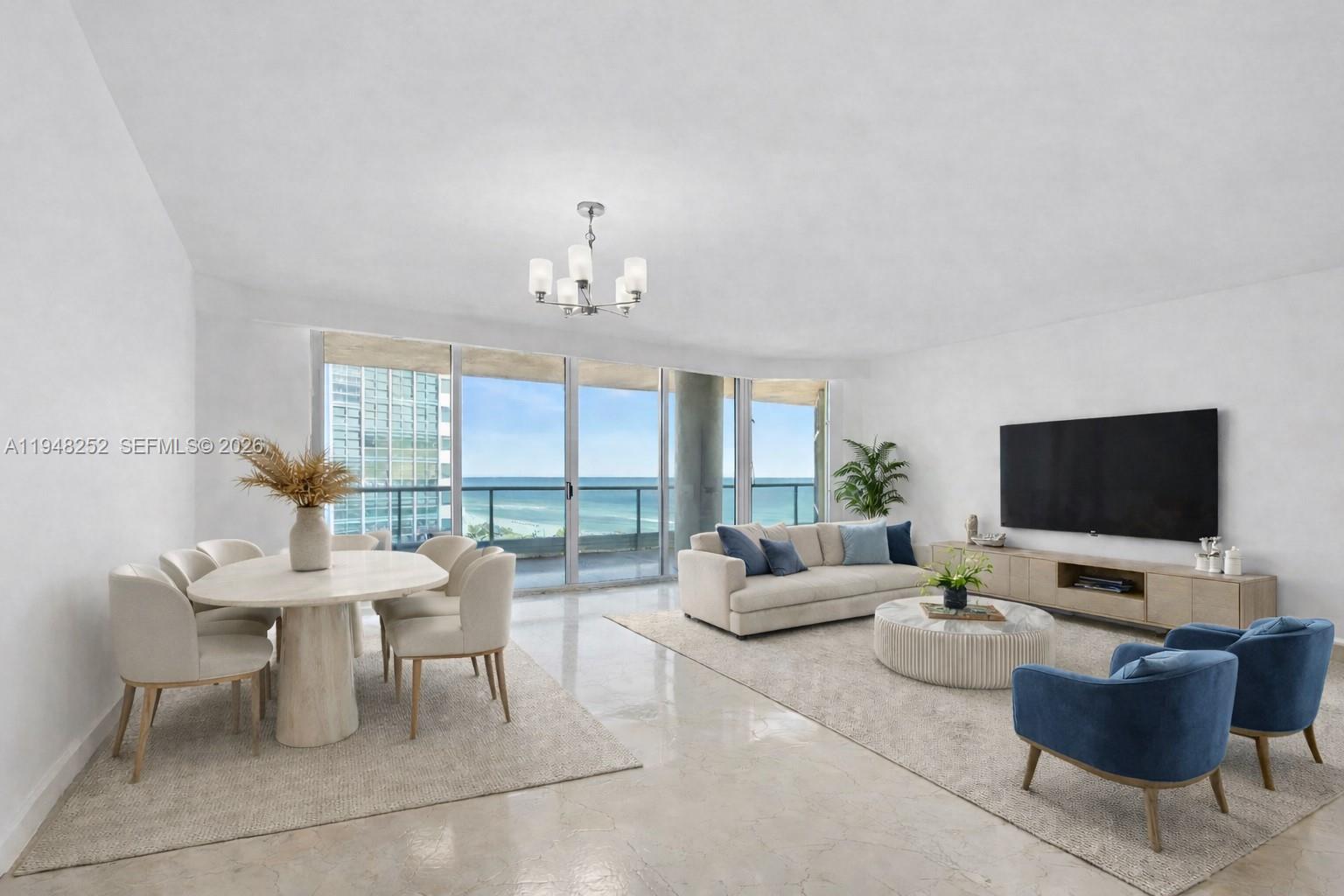 A bright living and dining area features neutral furniture, blue accent chairs, and ocean views — 5025 Collins Ave # 903, Miami Beach FL 33140, MIAMI BEACH, FL