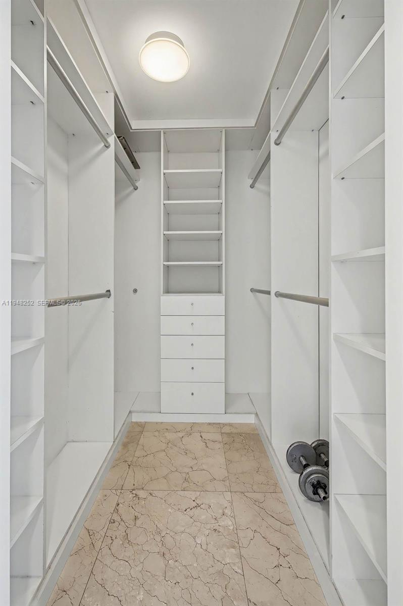 A walk-in closet features white shelving, a central drawer unit, and light-colored tile flooring — 5025 Collins Ave # 903, Miami Beach FL 33140, MIAMI BEACH, FL