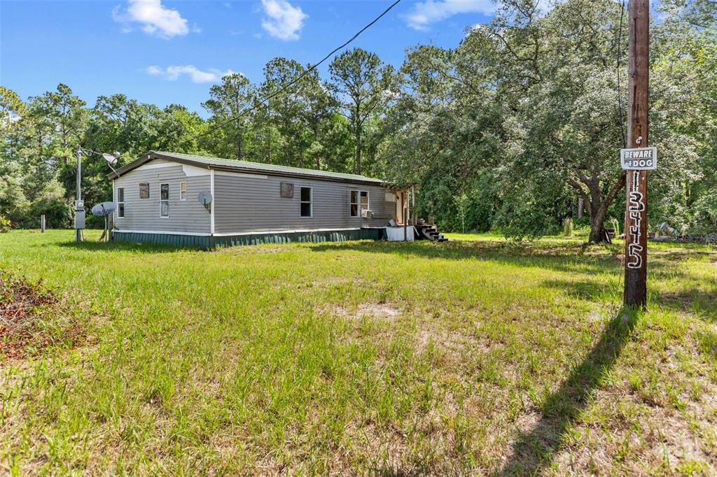 A single-story manufactured home sits on a grassy lot surrounded by trees — 13445 NE 156TH LANE, FORT MC COY, FL