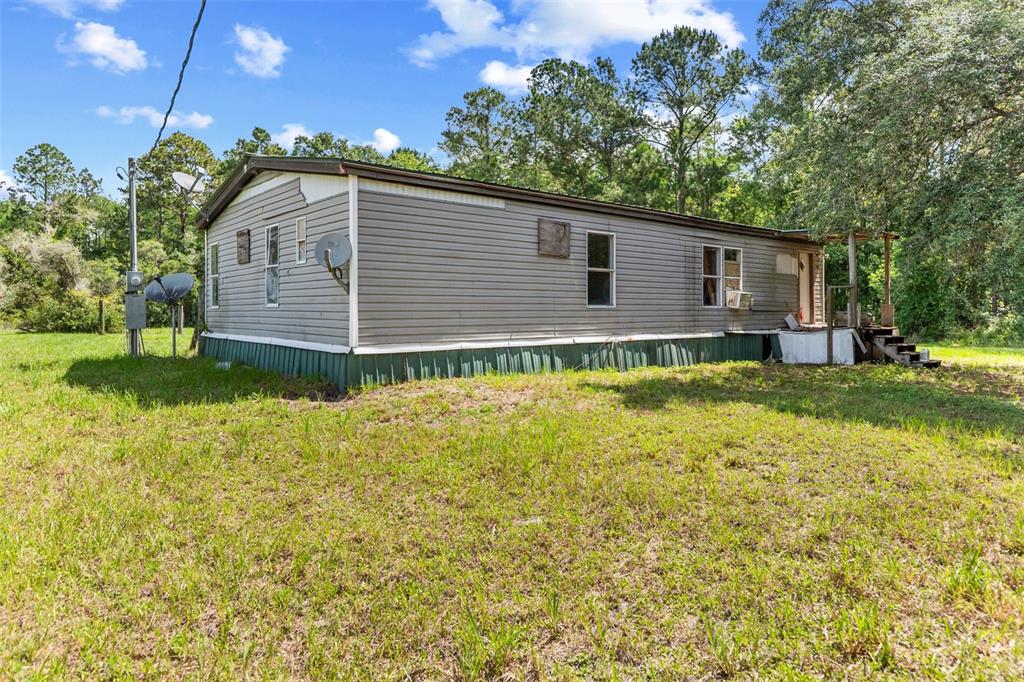 A single-story manufactured home with gray siding sits on a grassy lot with trees — 13445 NE 156TH LANE, FORT MC COY, FL