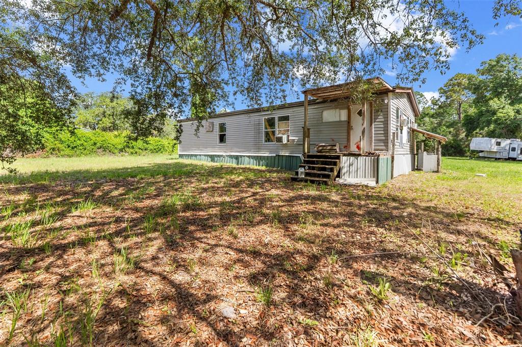 A single-story mobile home with gray siding sits on a grassy lot under large trees — 13445 NE 156TH LANE, FORT MC COY, FL