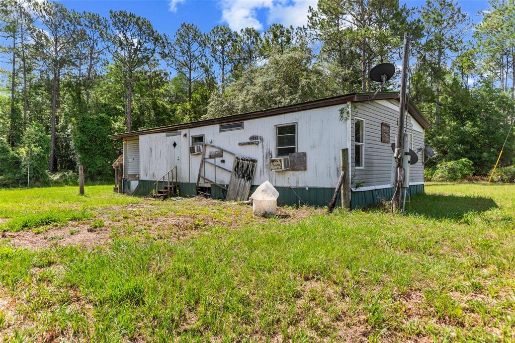 A weathered, single-wide mobile home sits on a grassy lot surrounded by pine trees — 13445 NE 156TH LANE, FORT MC COY, FL