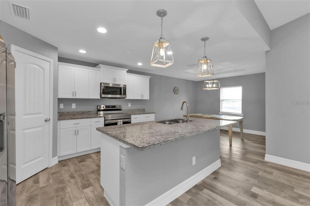 A kitchen features white cabinets, granite countertops, a center island, and light wood-look flooring — 14516 SAN DOMINGO BOULEVARD, PORT CHARLOTTE, FL