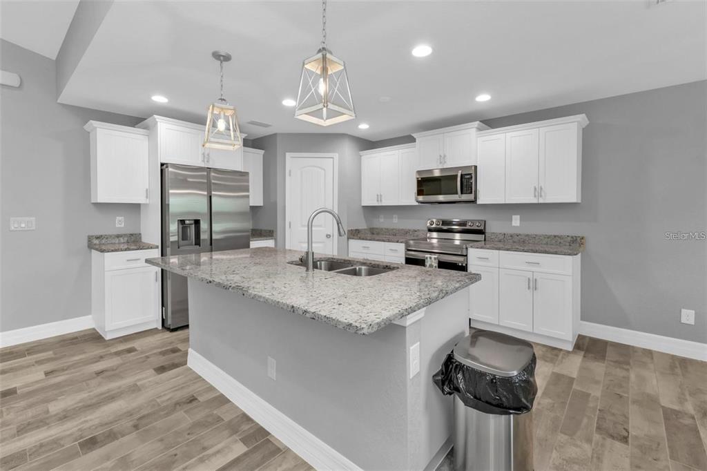 A modern kitchen features white cabinets, granite countertops, stainless steel appliances, and a central island — 14516 SAN DOMINGO BOULEVARD, PORT CHARLOTTE, FL