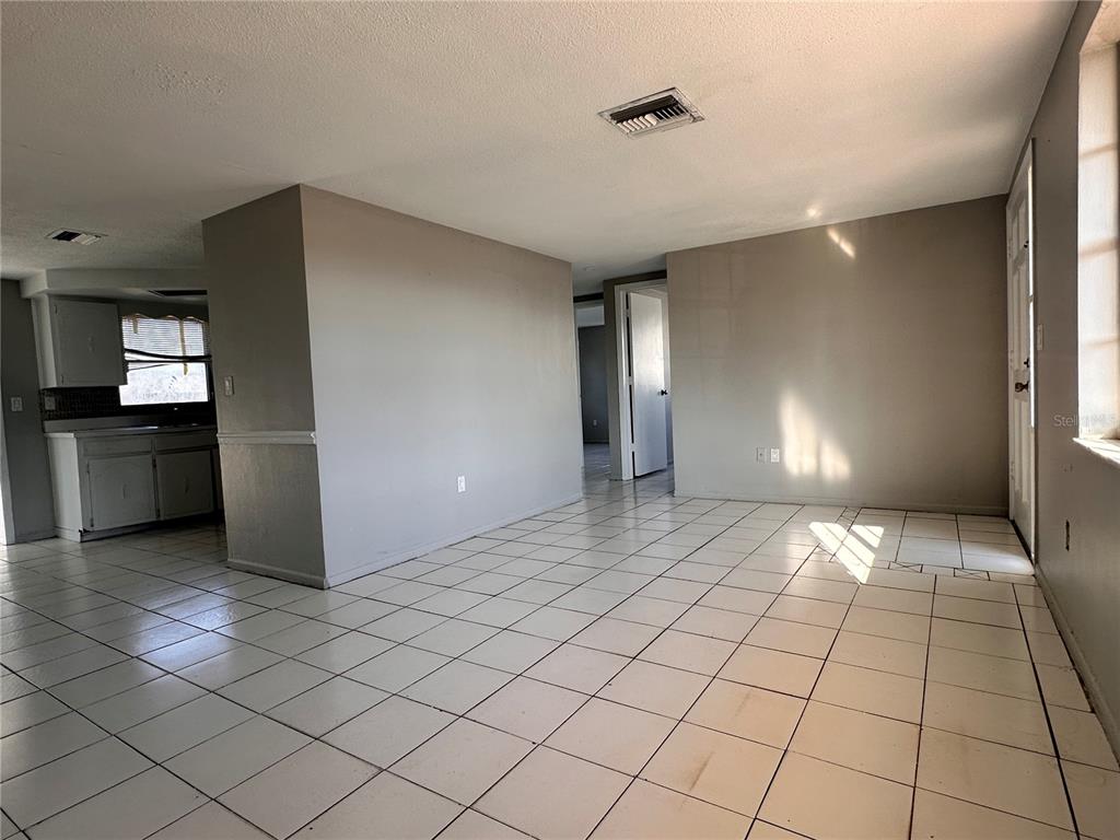An interior view shows a room with white tile flooring, light gray walls, and a kitchen — 3215 BRIGHT DRIVE, HOLIDAY, FL