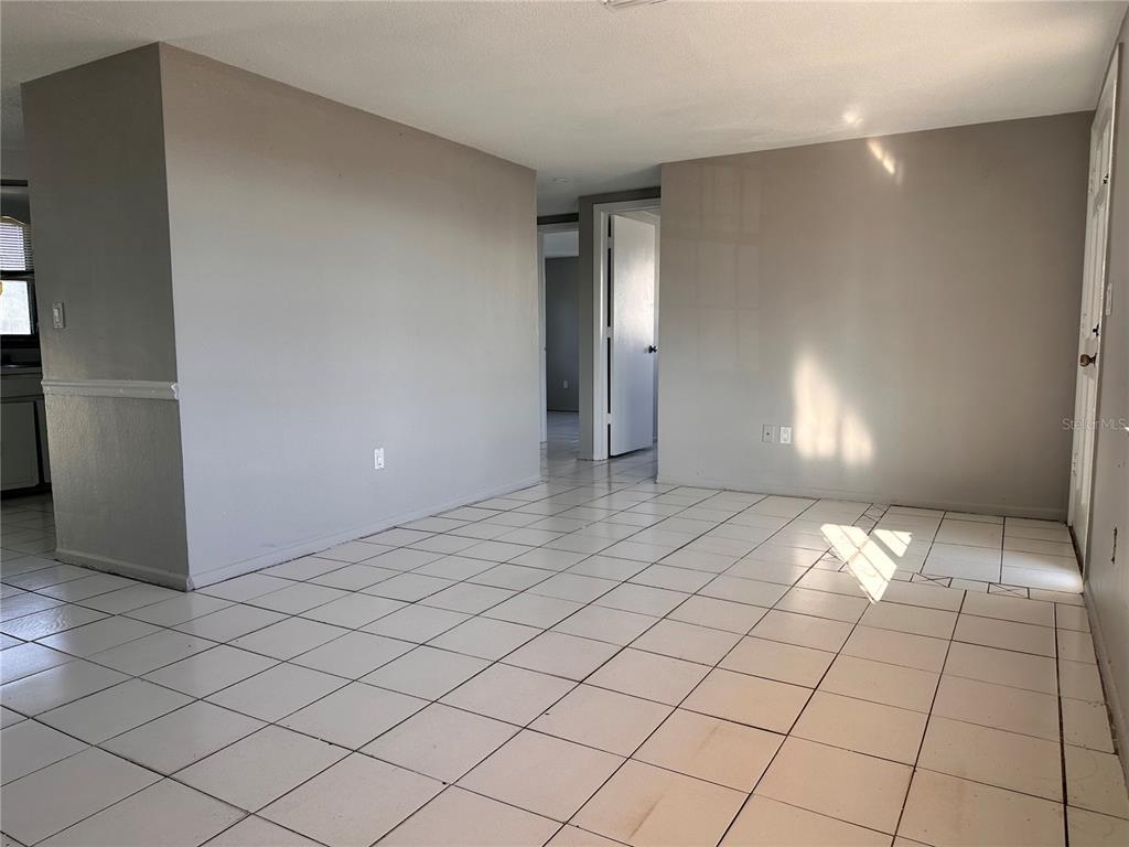 An empty room with light gray walls and white tiled flooring leads to a hallway — 3215 BRIGHT DRIVE, HOLIDAY, FL