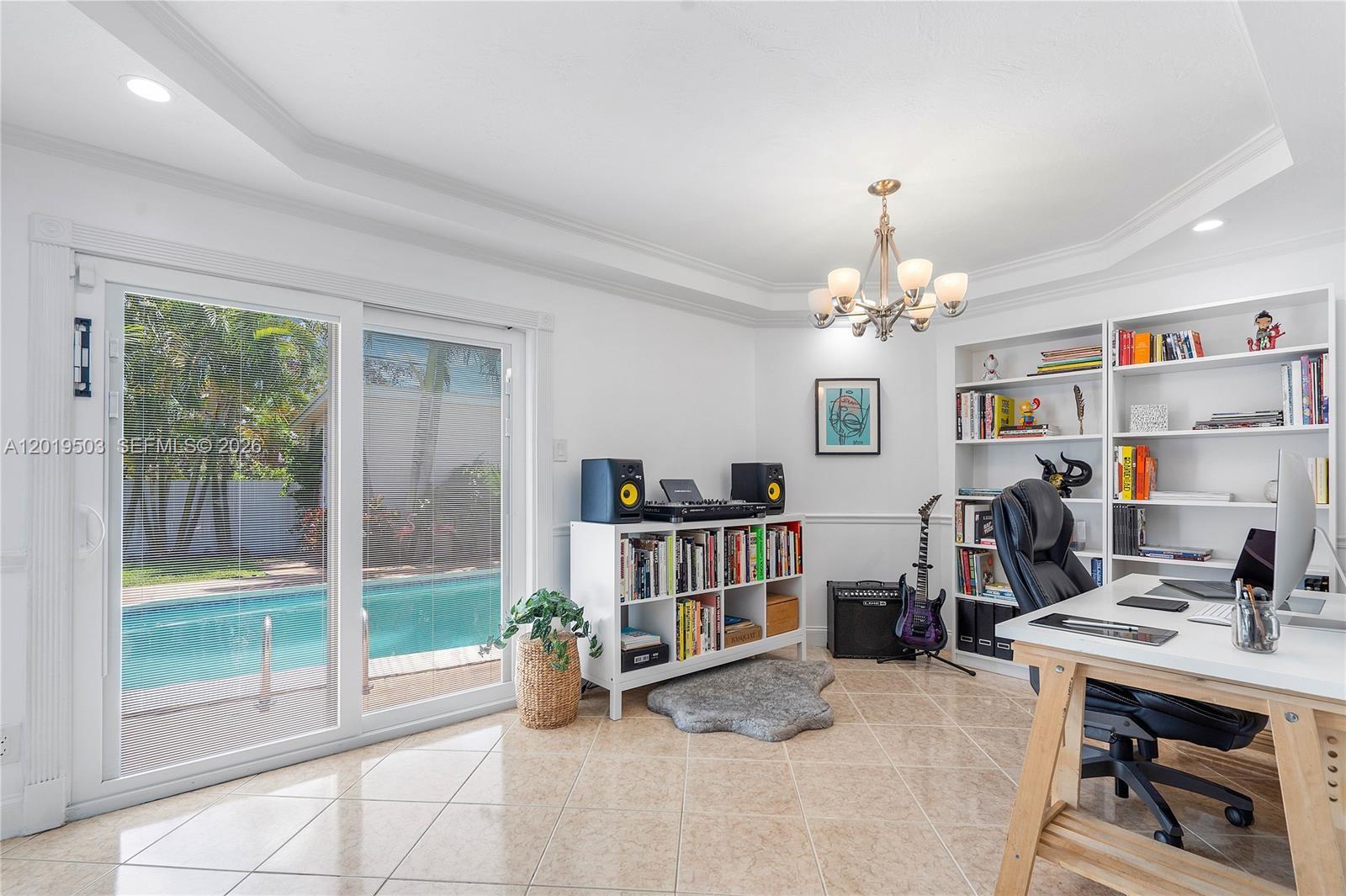A home office features a desk, bookshelves, a guitar, and sliding doors overlooking a pool — 3021 N 72nd Way, Hollywood FL 33024, HOLLYWOOD, FL