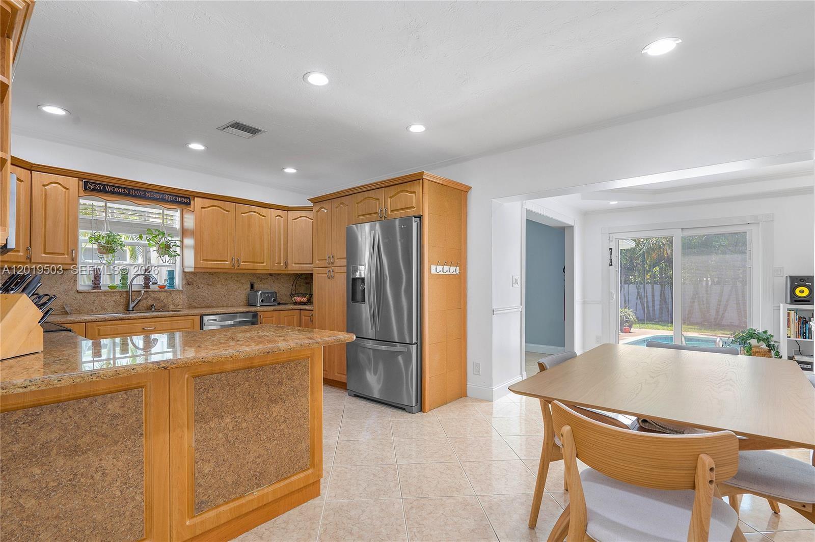 A kitchen with wood cabinets, granite countertops, and a dining area overlooking a backyard pool — 3021 N 72nd Way, Hollywood FL 33024, HOLLYWOOD, FL