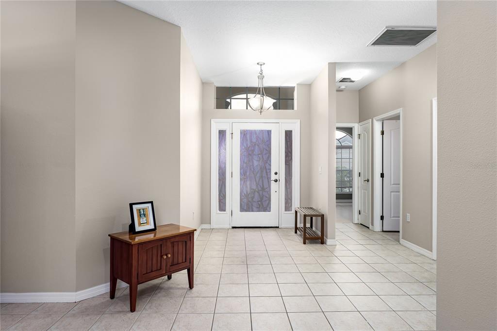 A tiled entryway features a white front door with sidelights, a chandelier, and wooden furniture — 6508 ROCK BRIDGE LANE, ELLENTON, FL