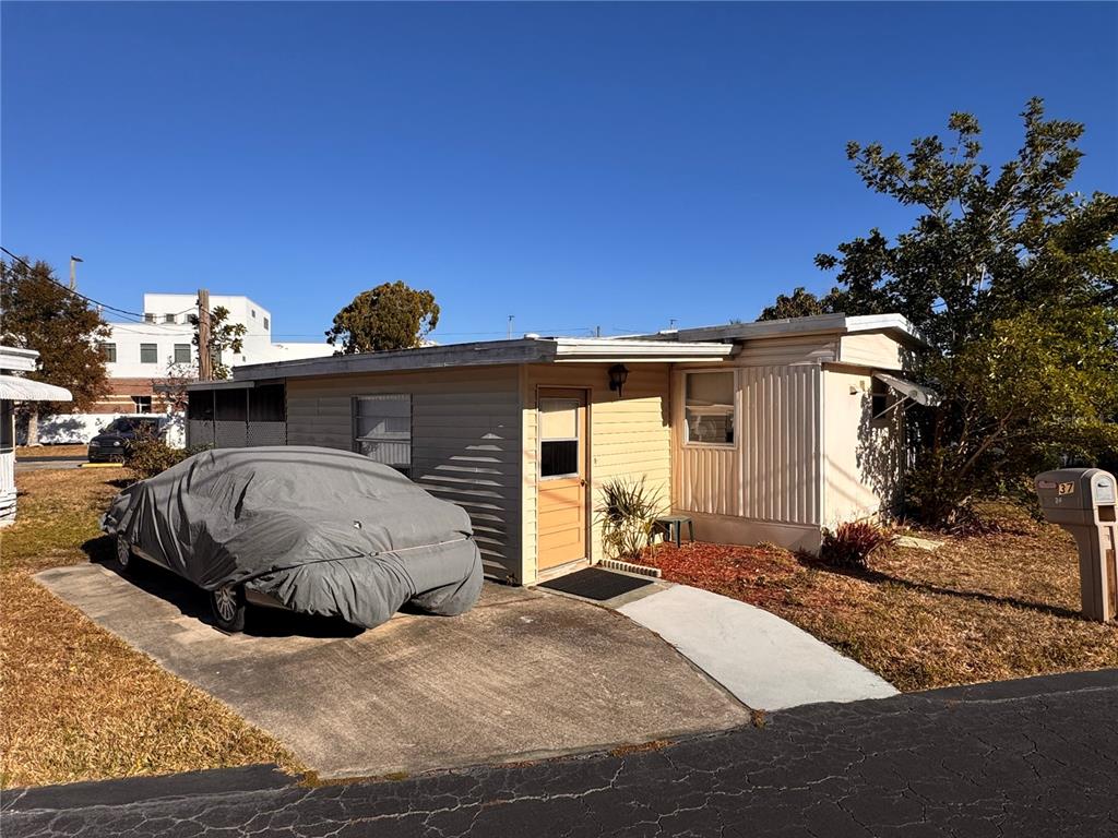 A single-story mobile home with a covered car and a concrete driveway under a blue sky — 6720 PARK BOULEVARD N UNIT 37, PINELLAS PARK, FL