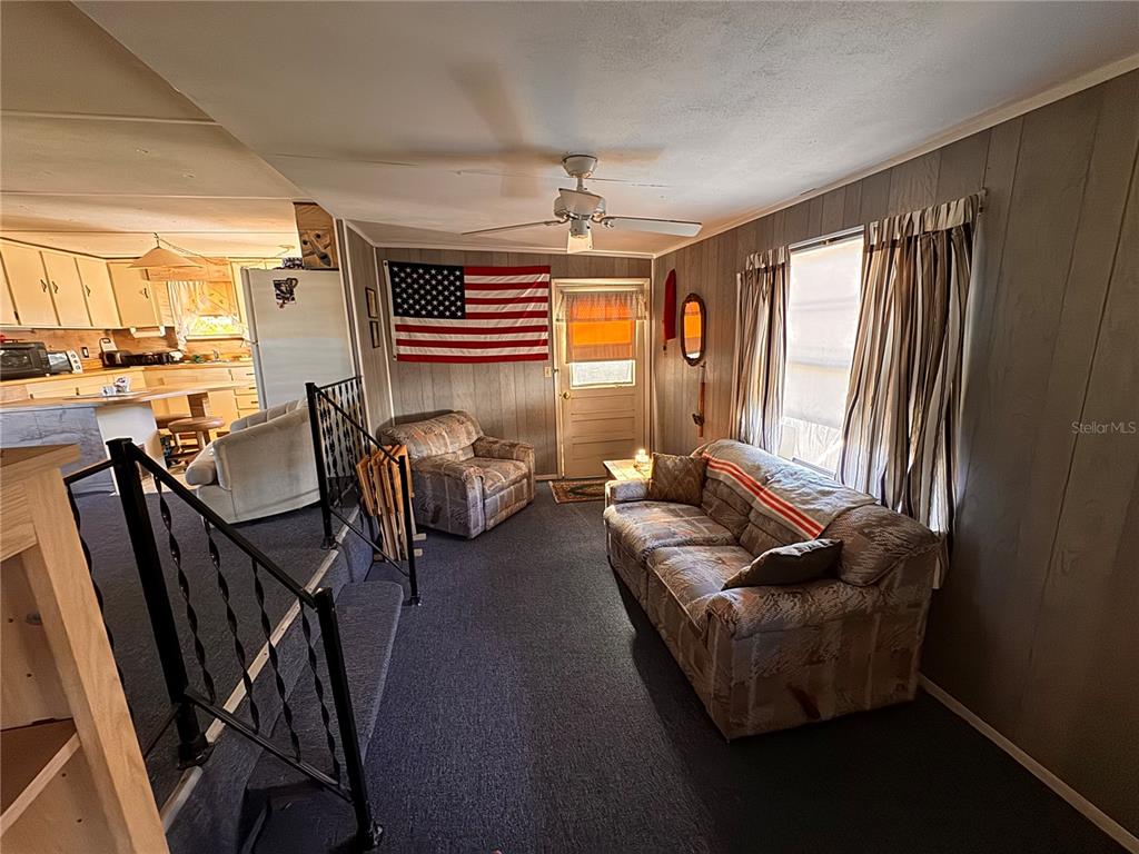 A living room with wood-paneled walls, a patterned sofa, an armchair, and an American flag — 6720 PARK BOULEVARD N UNIT 37, PINELLAS PARK, FL