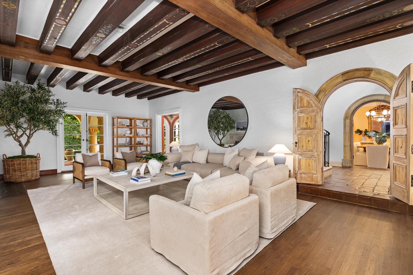 A living room features exposed wood-beamed ceilings, arched doorways, and neutral-toned furniture on a rug — 124 Brazilian Avenue, Palm Beach FL 33480, PALM BEACH, FL