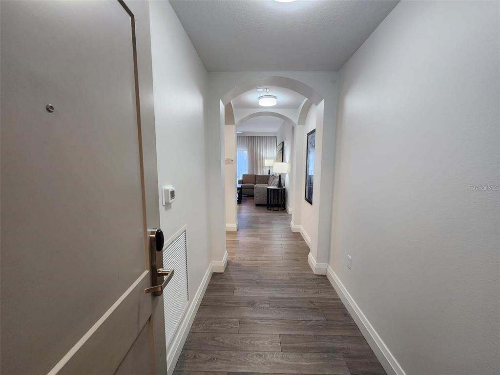 A hallway with wood-look flooring leads to a living area with an arched ceiling detail — 14501 GROVE RESORT AVENUE UNIT 3401, WINTER GARDEN, FL