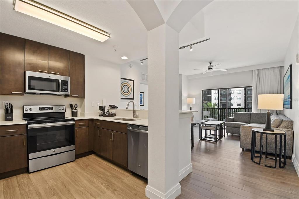 A kitchen with dark wood cabinets and stainless steel appliances opens into a living area — 14501 GROVE RESORT AVENUE UNIT 3401, WINTER GARDEN, FL