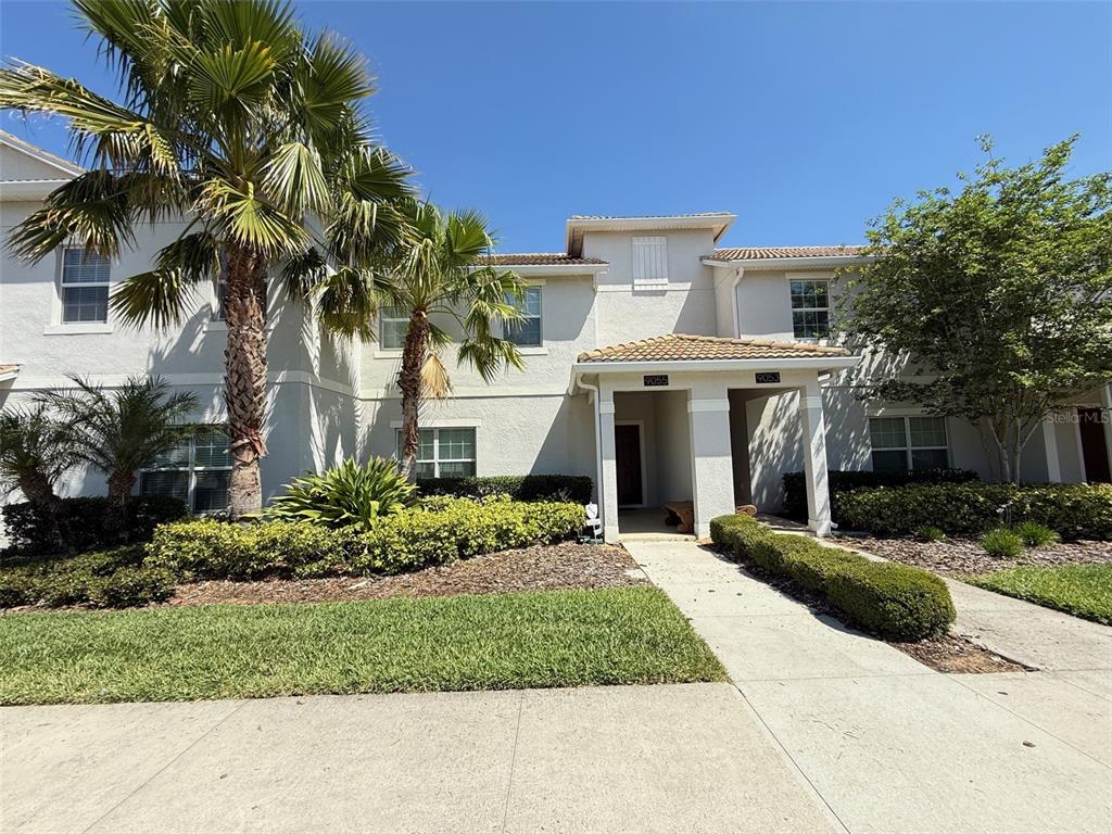 A two-story stucco townhouse features a covered entryway, palm trees, and a landscaped front yard — 9055 DOGLEG DRIVE, DAVENPORT, FL