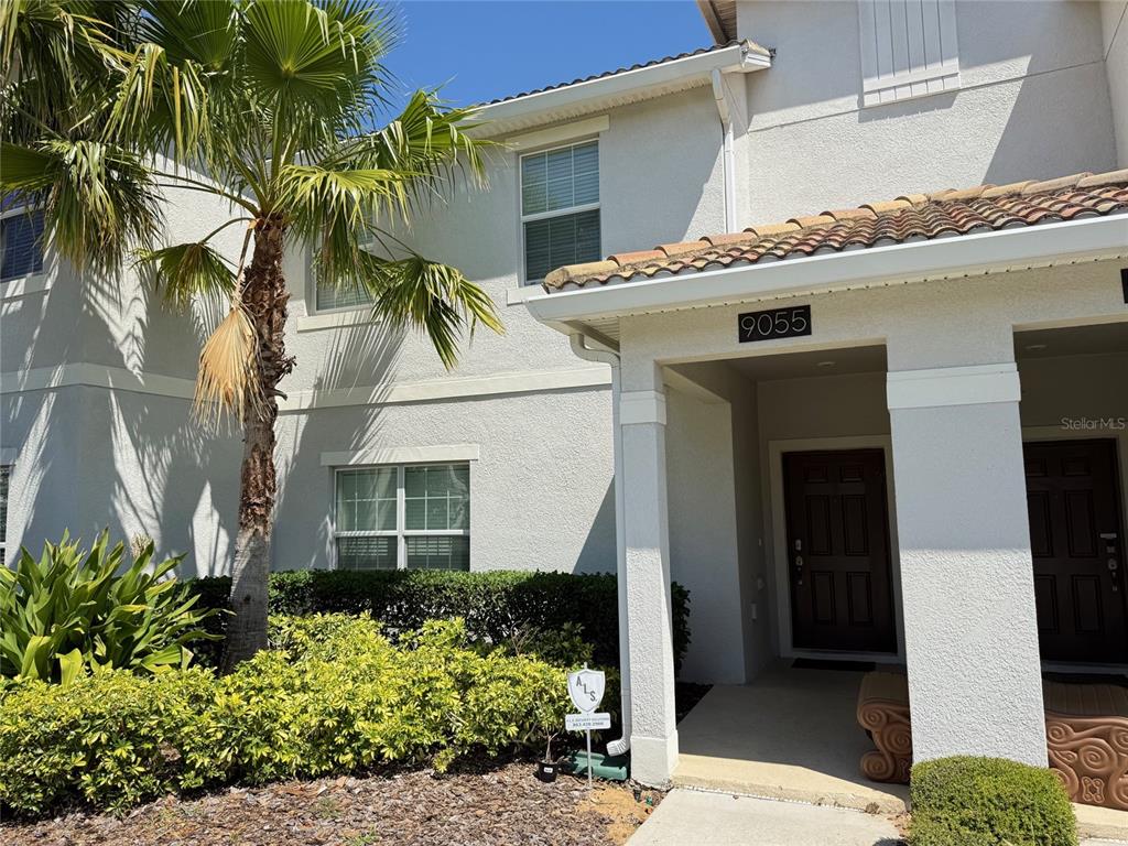 A two-story stucco townhouse exterior features a palm tree, a covered entryway, and landscaping — 9055 DOGLEG DRIVE, DAVENPORT, FL