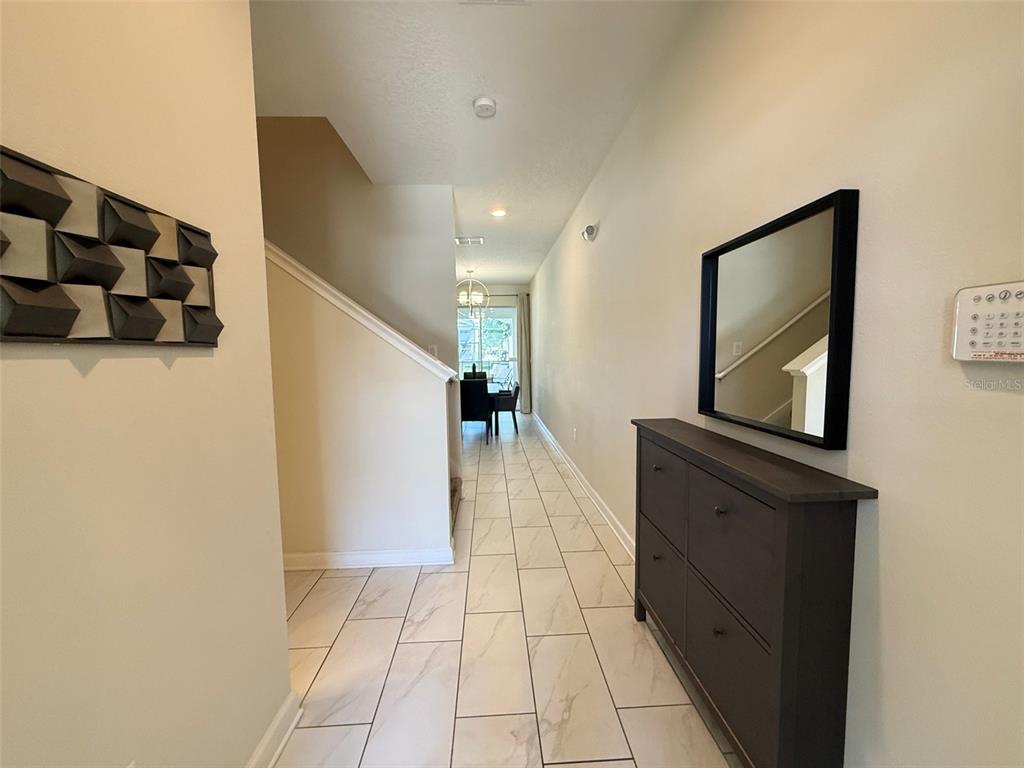A tiled hallway features a dark wood shoe cabinet, a wall mirror, and a staircase — 9055 DOGLEG DRIVE, DAVENPORT, FL
