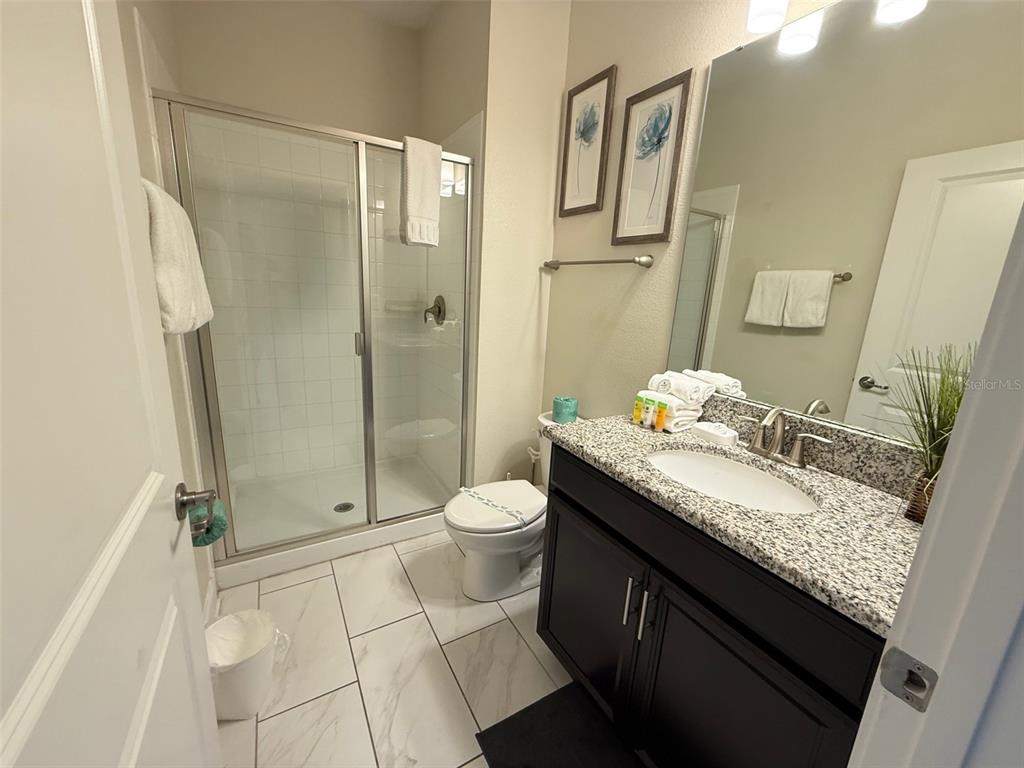A bathroom features a glass-enclosed shower, a dark vanity with granite countertop, and tiled floors — 9055 DOGLEG DRIVE, DAVENPORT, FL