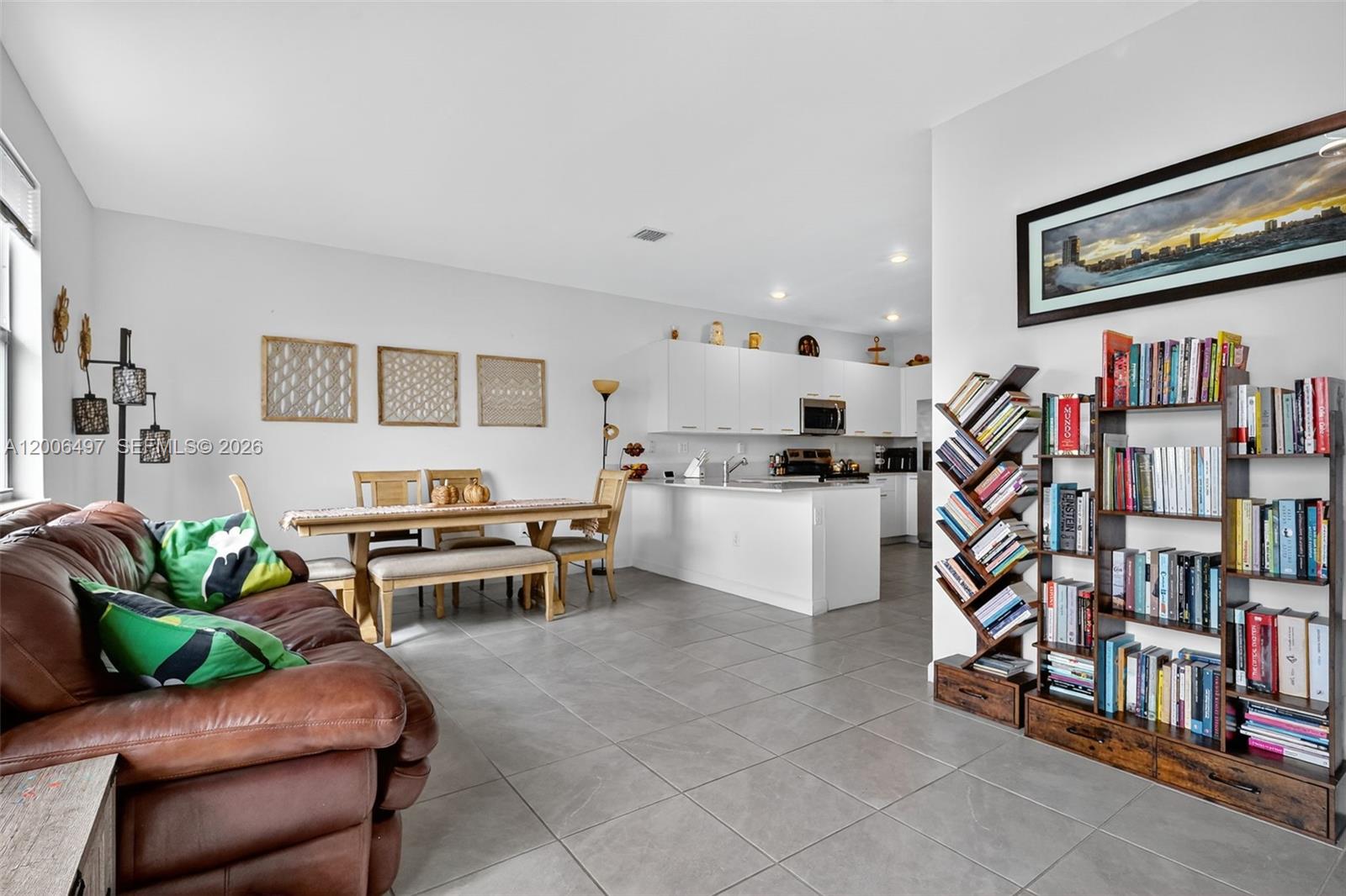 An open-concept living and dining area features tile flooring, white cabinetry, and a large bookshelf — 12936 NW 22nd Pl, Miami FL 33167, MIAMI, FL