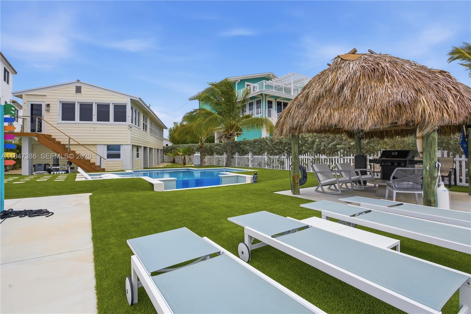 A backyard features a swimming pool, artificial turf, lounge chairs, and a thatched-roof tiki hut — 235 Tavernier Dr, Key Largo FL 33070, KEY LARGO, FL